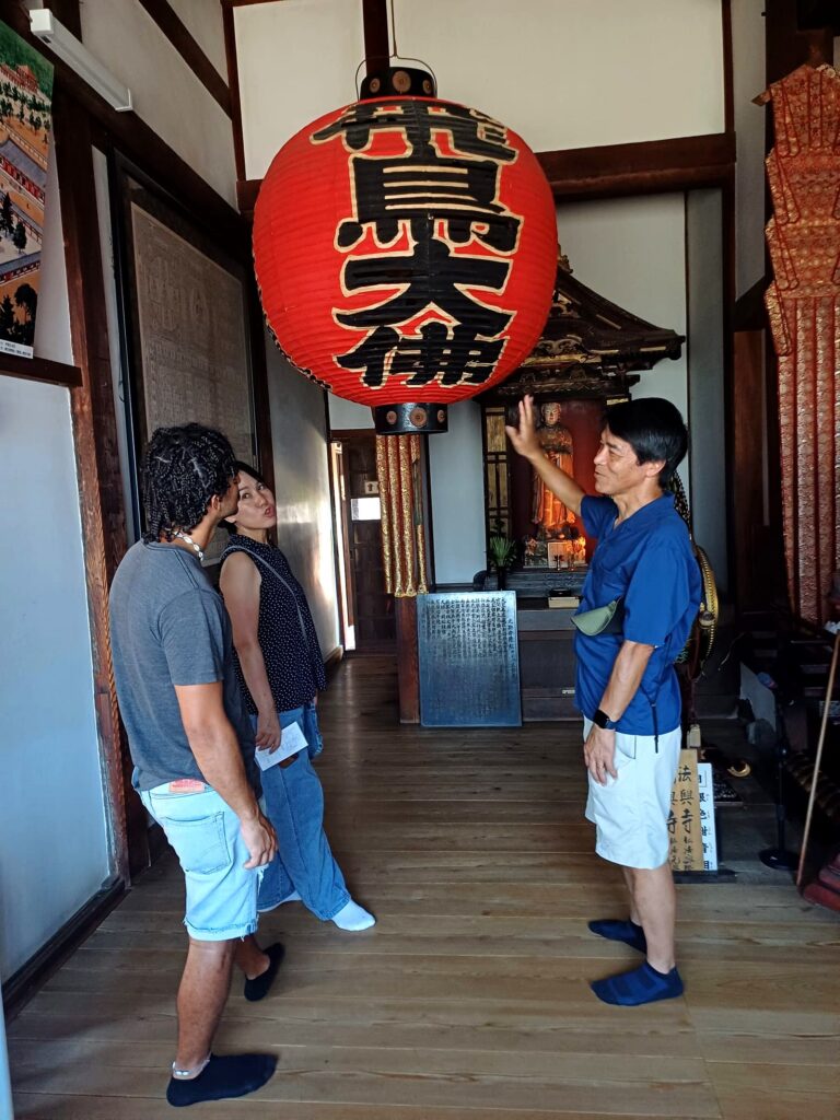 Guía local explicando la historia de un templo tradicional a viajeros internacionales en Asuka, Nara rural